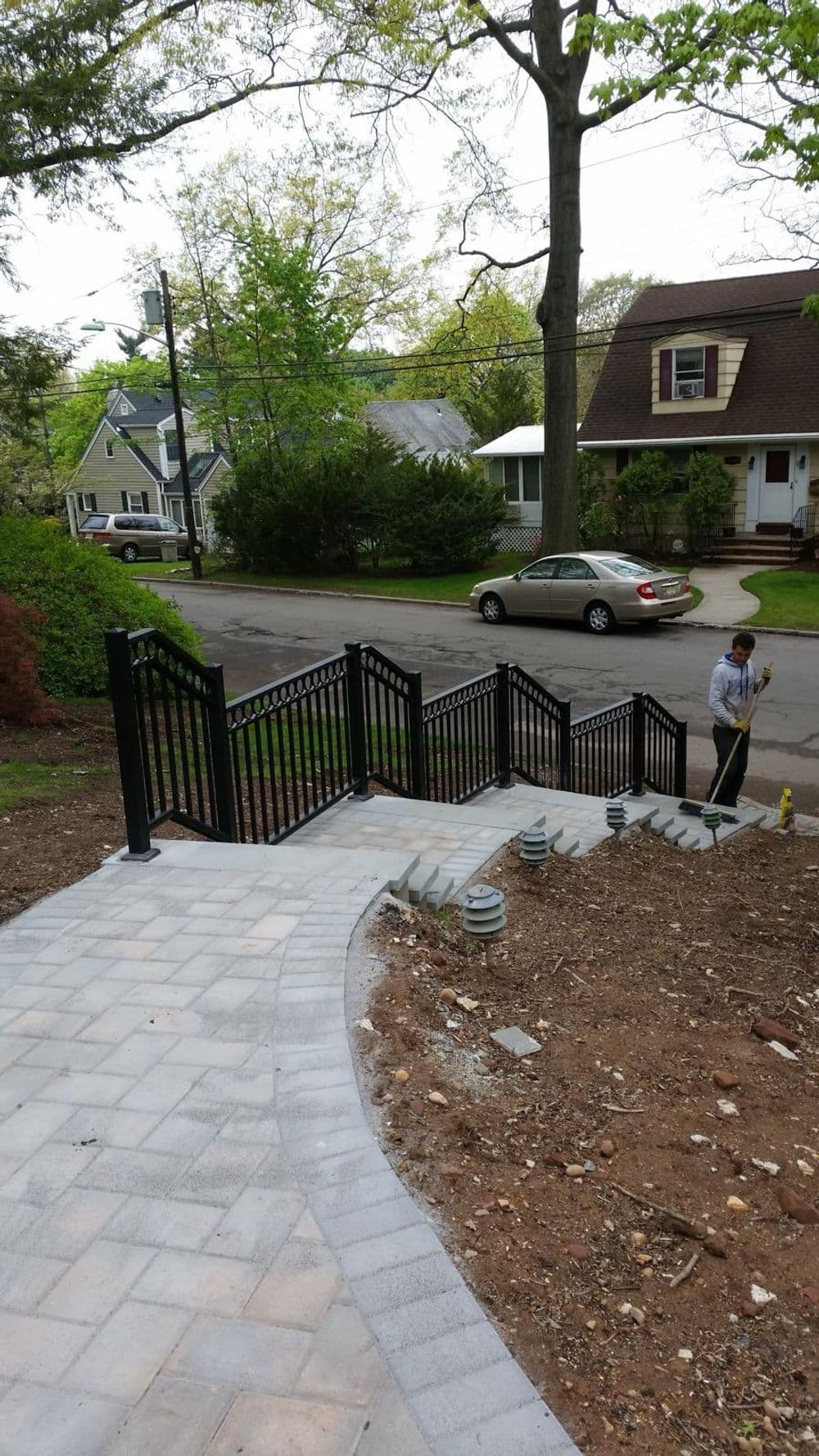Concrete walkway with black railings leading to a landscaped yard and residential street.