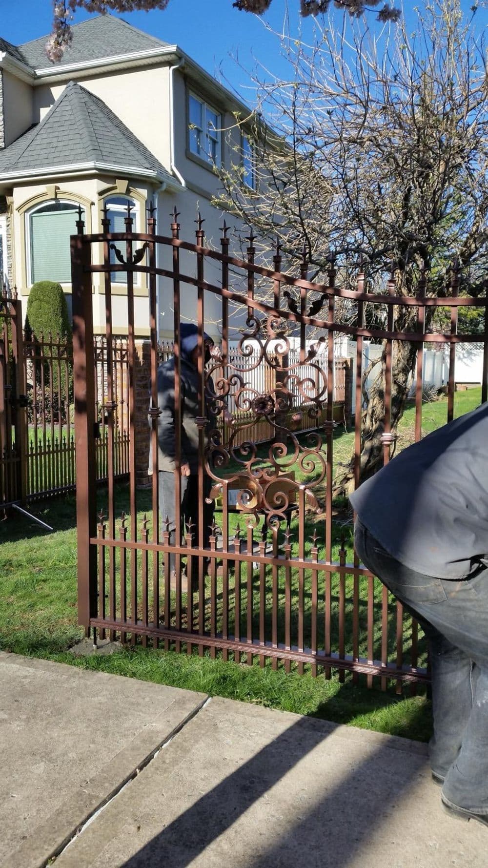 Maintenance of an ornate metal gate in front of a house with a clear blue sky.