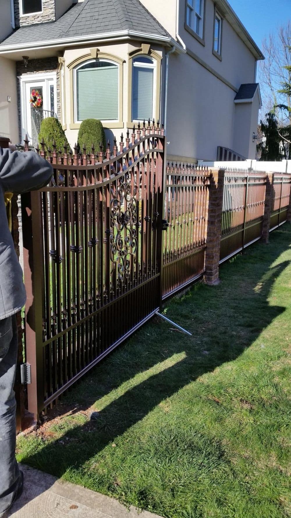 Elegant metal fence installation with decorative elements in front of a house and landscaped lawn.