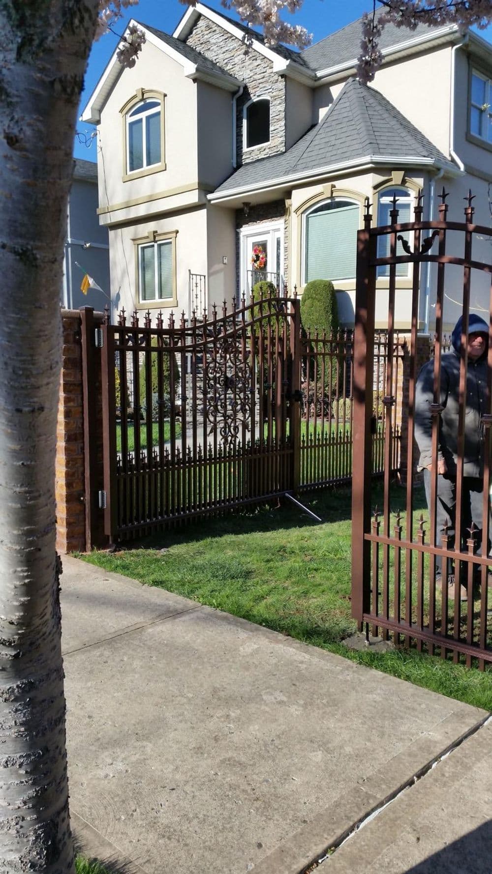Brown wrought iron gate with a house and landscaped yard in the background on a sunny day.