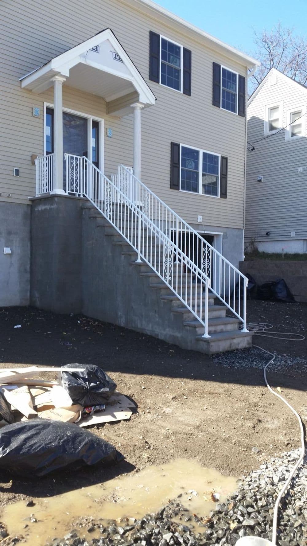 Newly constructed building entrance with white railing and concrete steps, surrounded by gravel.