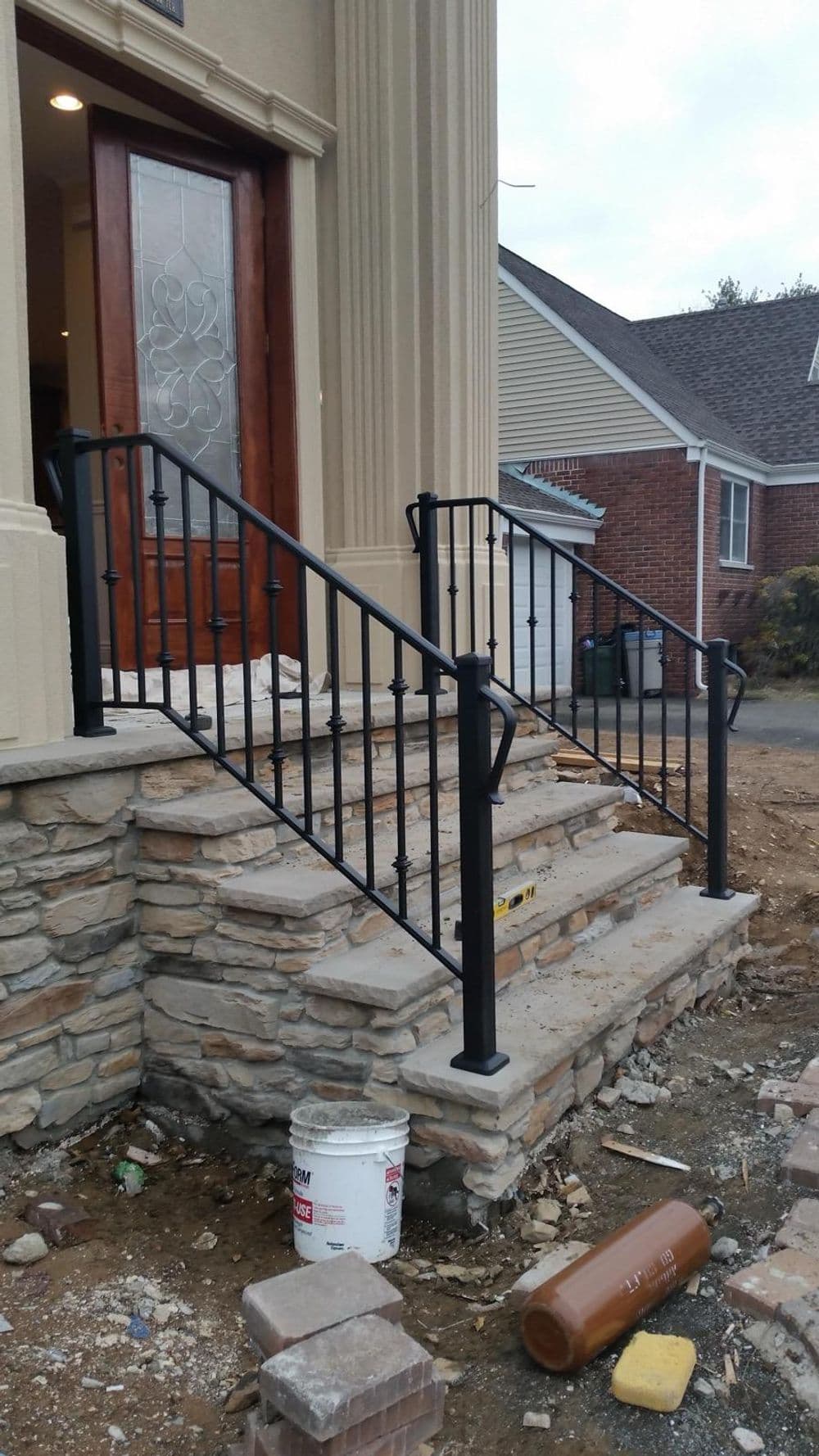 Black wrought iron railing on stone steps leading to a home entrance under construction.