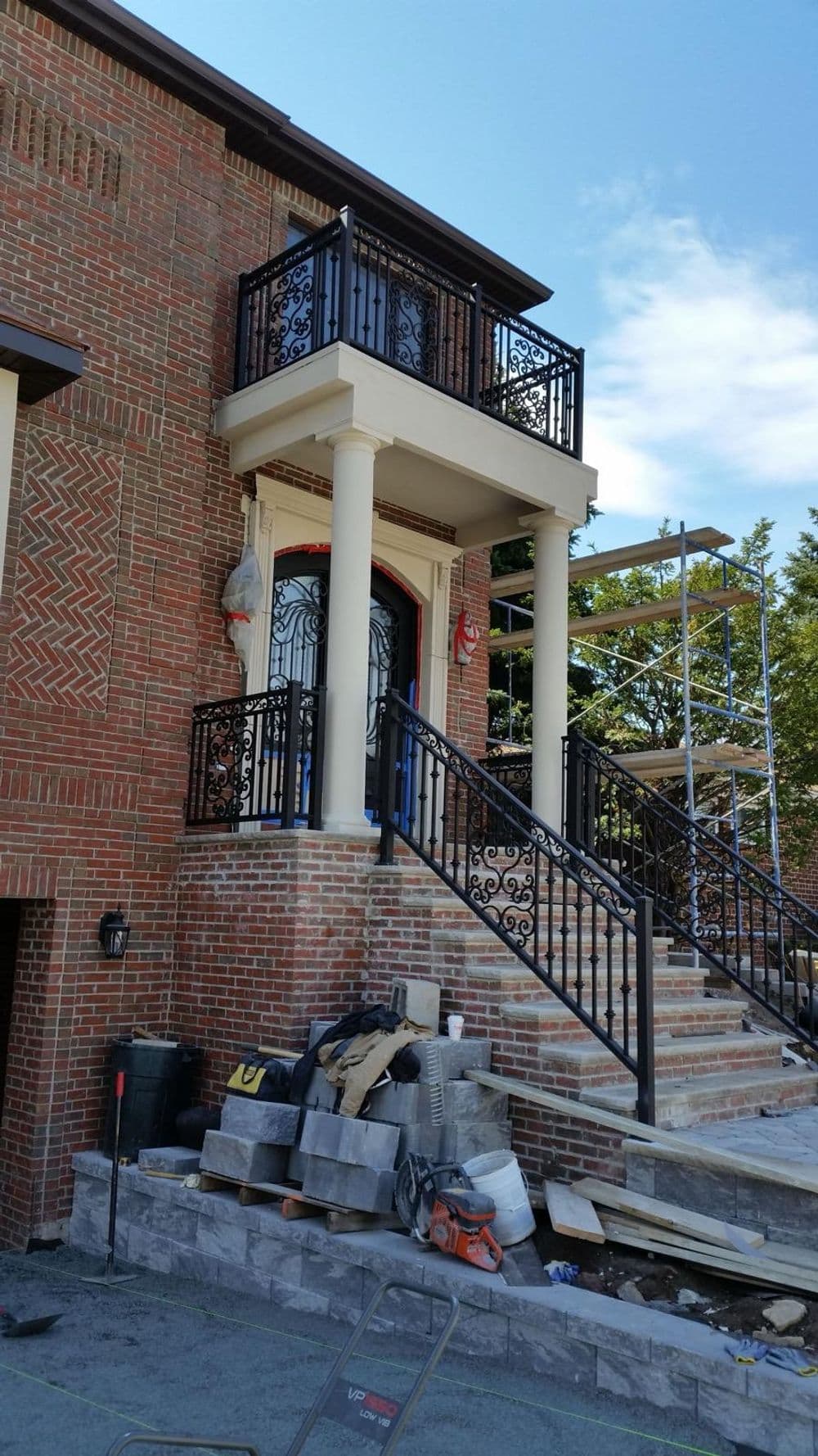 Modern home entrance with decorative balcony and brick exterior, under construction with tools nearby.