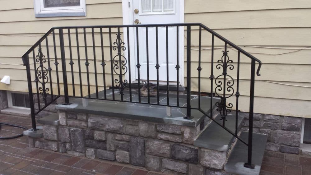 Wrought iron railing on a stone porch with steps leading to a white door.