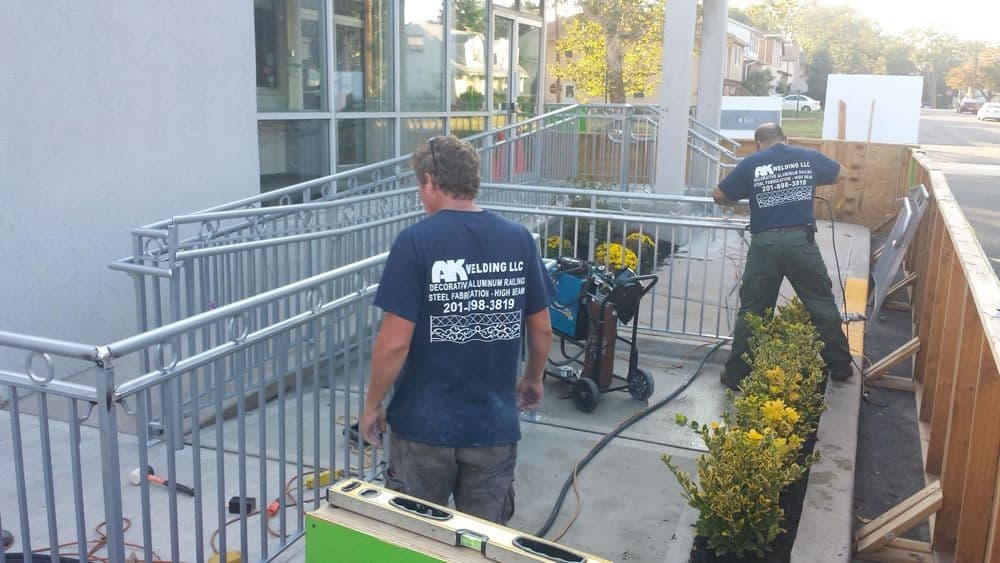 Workers installing metal railings outside a commercial building, surrounded by flowers and tools.
