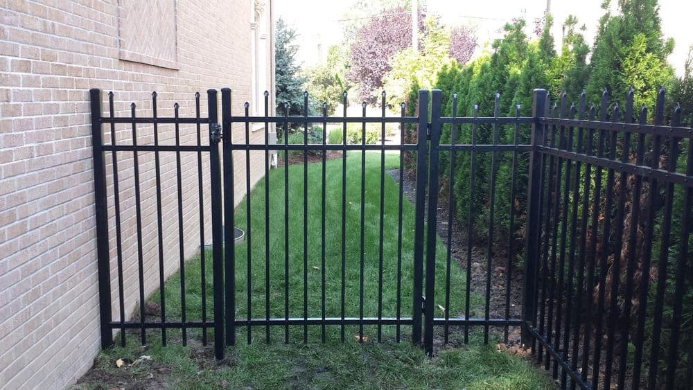 Black metal gate opening to a well-maintained grassy area between two fences.