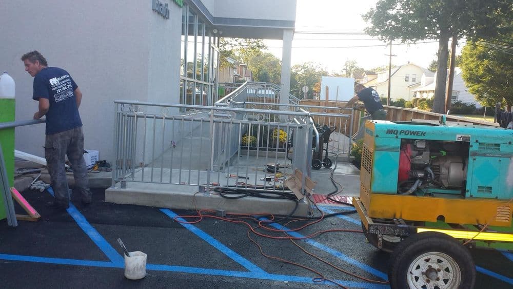Construction workers installing a wheelchair ramp outside a building with machinery.