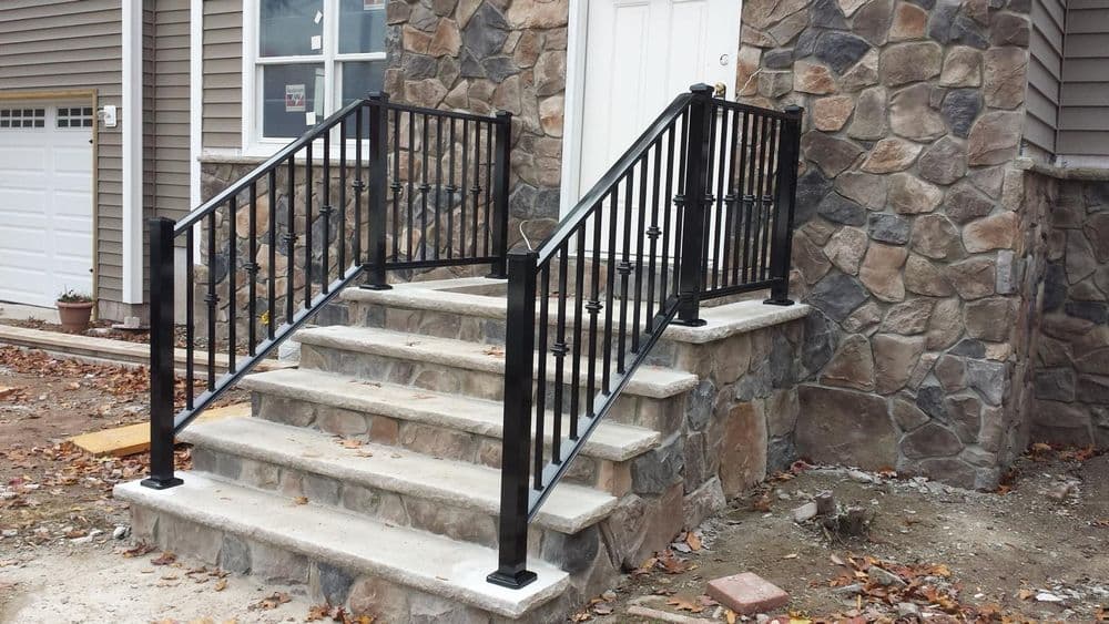 Black metal railing on stone steps leading to a front door of a home.