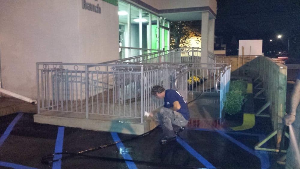 Worker applying black sealant to a freshly painted handicap-accessible ramp at night.
