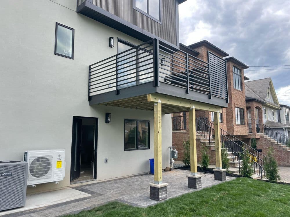 Modern home with a balcony supported by wooden posts, grassy yard, and air conditioning unit.