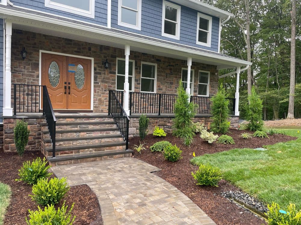 Front entrance of a blue stone house with wooden doors, landscaped garden, and pathway.