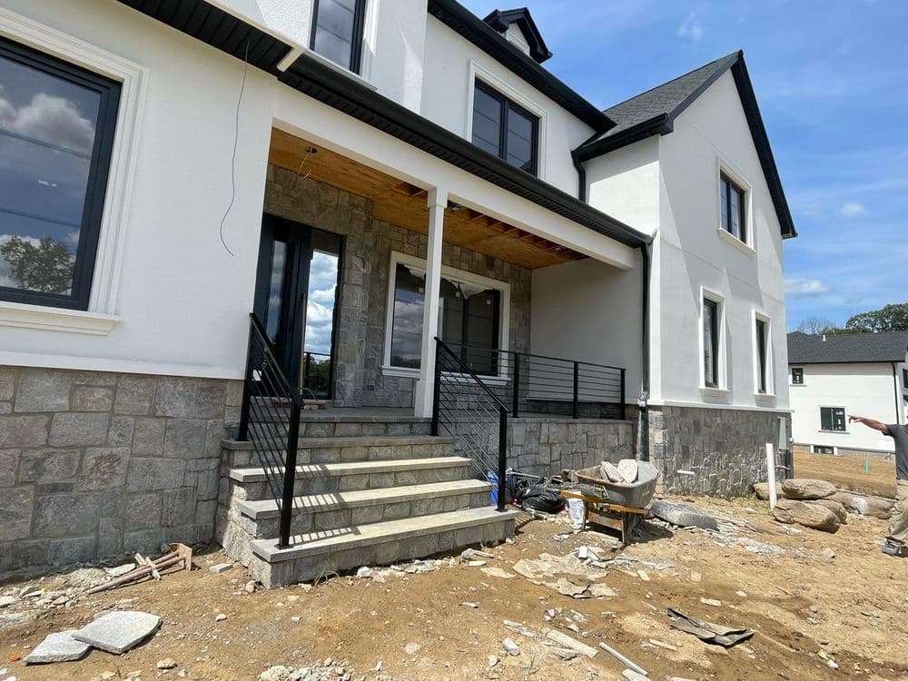 Modern home under construction, featuring stone steps and a stylish façade.