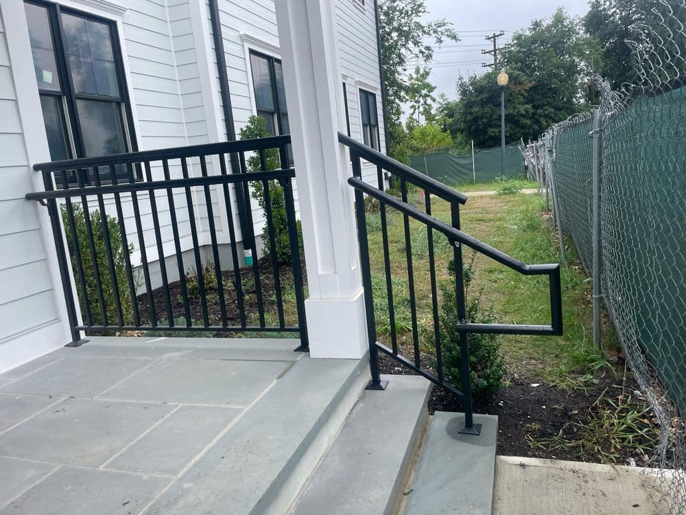 Accessible metal handrail alongside a wide concrete step leading to a landscaped area.