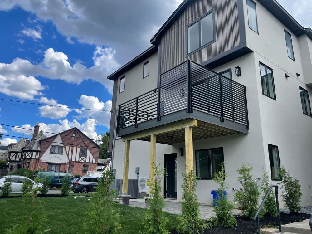 Modern two-story house with balcony, surrounded by greenery and blue sky.