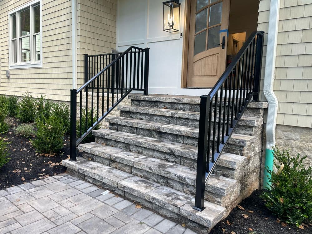 Black metal railings on stone steps leading to a modern home entrance with landscaping.