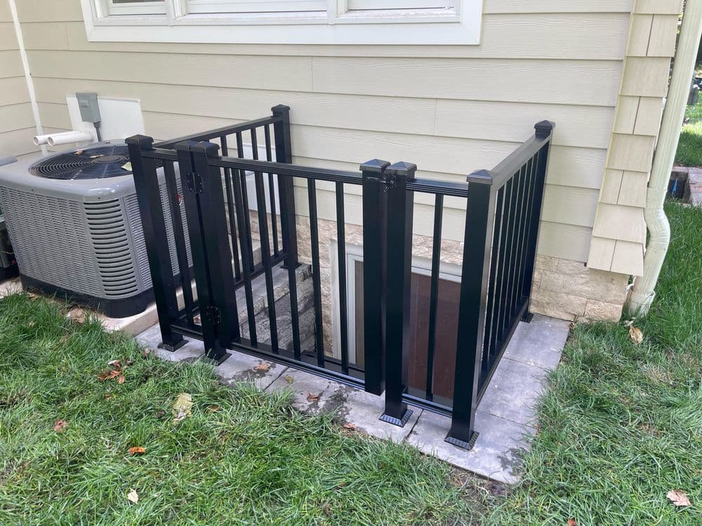Black metal railing exterior stairway leading to a basement entrance near an outdoor AC unit.