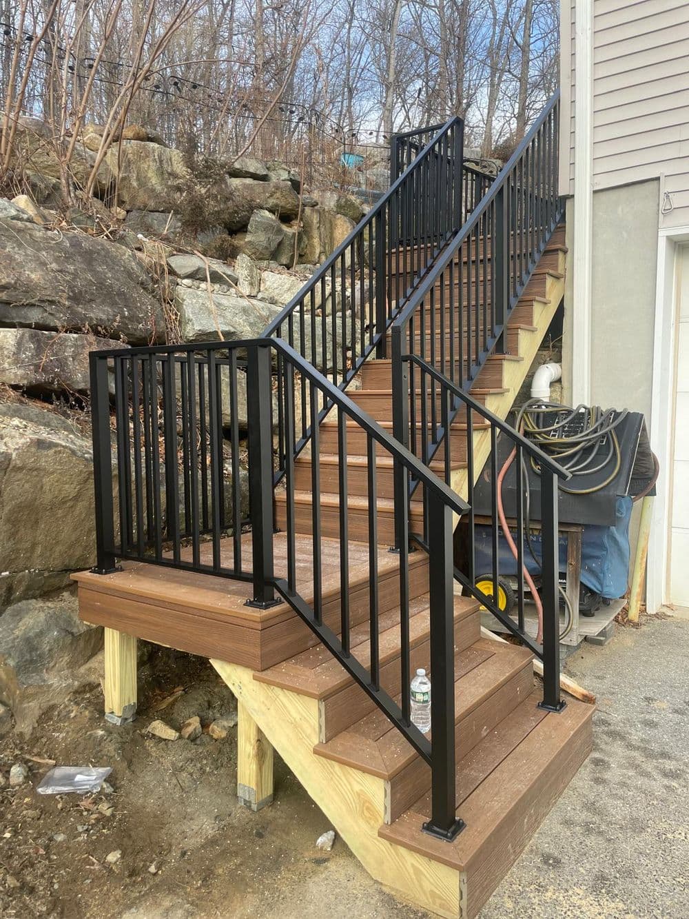Sturdy wooden staircase with black railing built against a rocky landscape.
