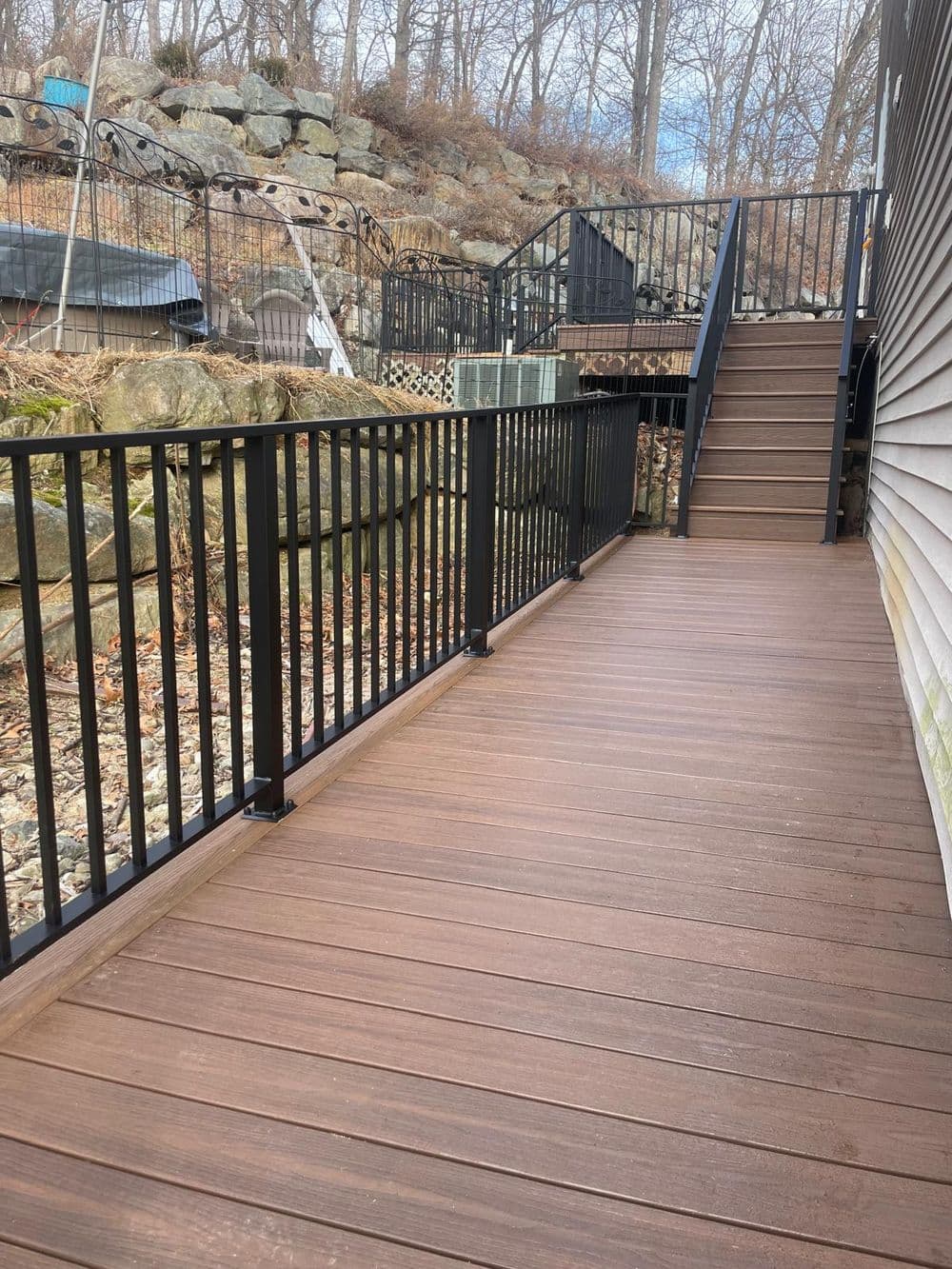 Modern wooden deck with black railing and stone landscape in a wooded area.
