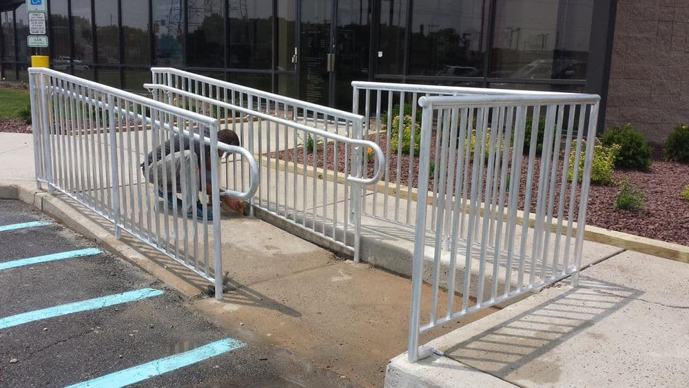 Worker installing metal railings for wheelchair access ramp outside a building.