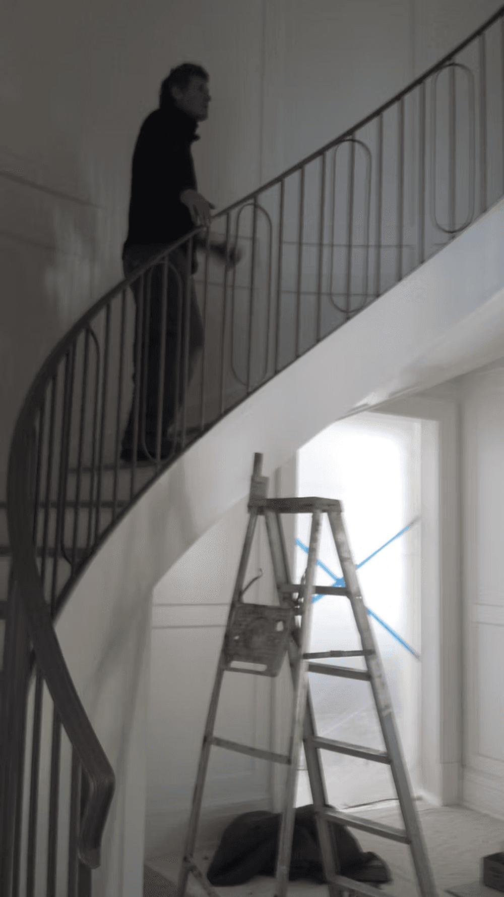 Man working on a curved staircase with a ladder in a bright, unfinished home interior.