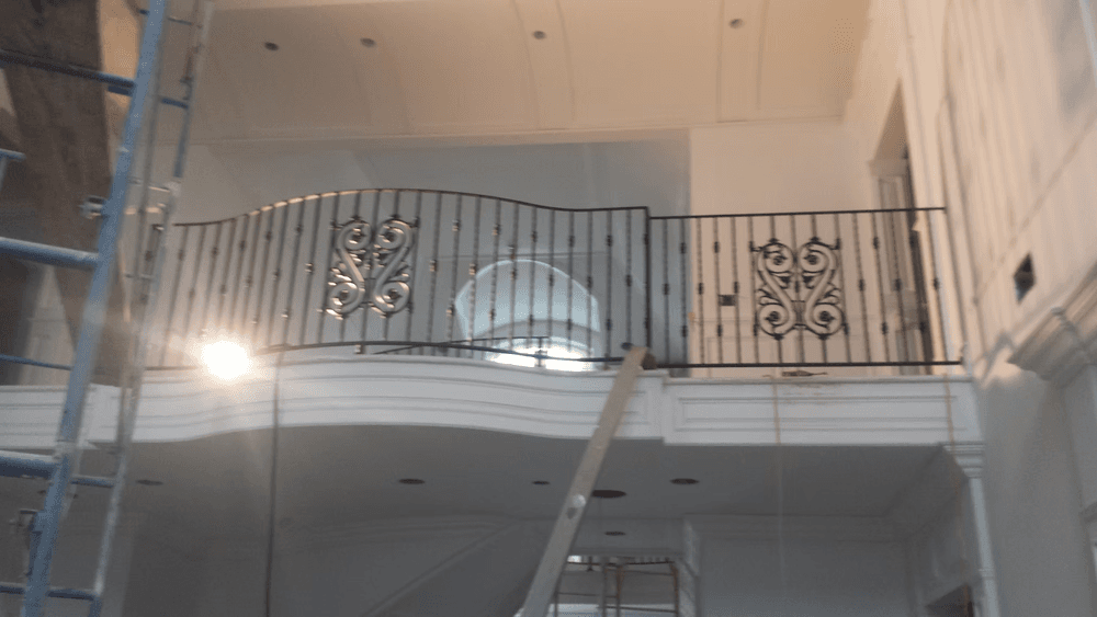 Interior view of a staircase railing with intricate black metal design. Renovation underway.