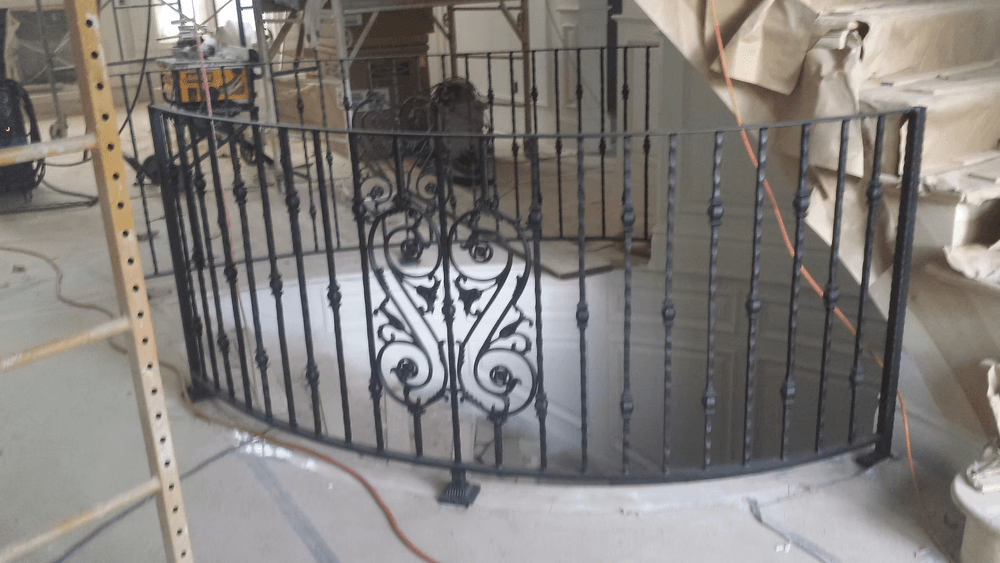 Wrought iron railing with ornate design in a partially constructed interior space.