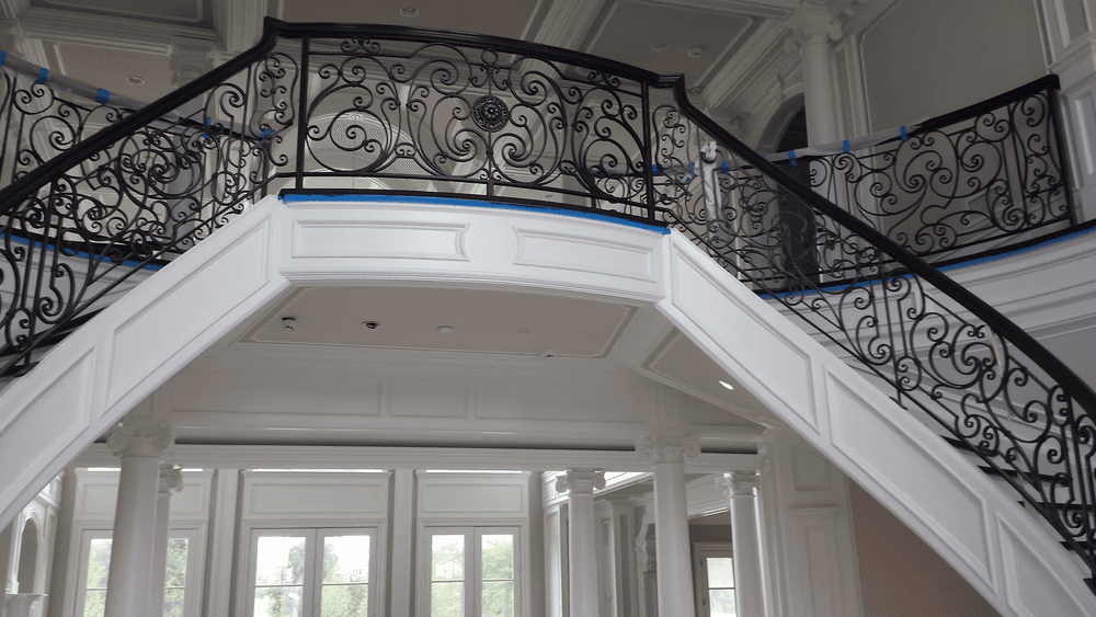 Elegant curved staircase with intricate black wrought iron railing in a luxury home interior.