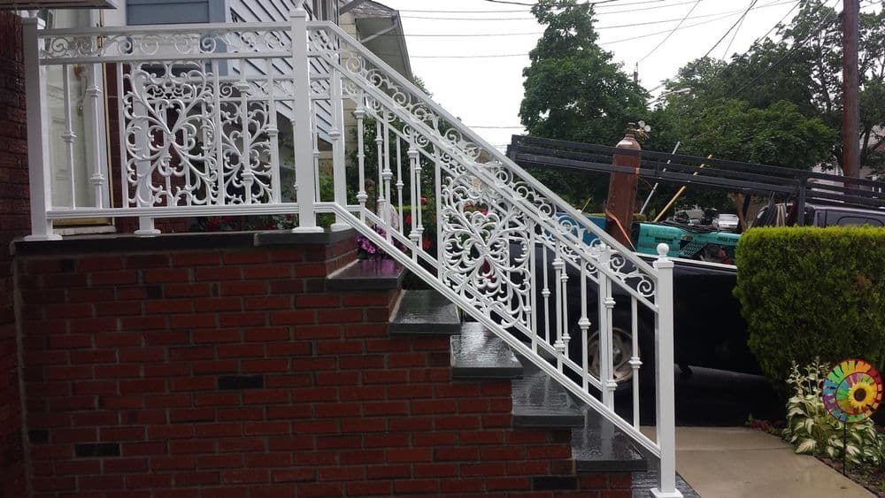 Elegant white wrought iron railing on brick steps, enhancing home exterior with floral accents.