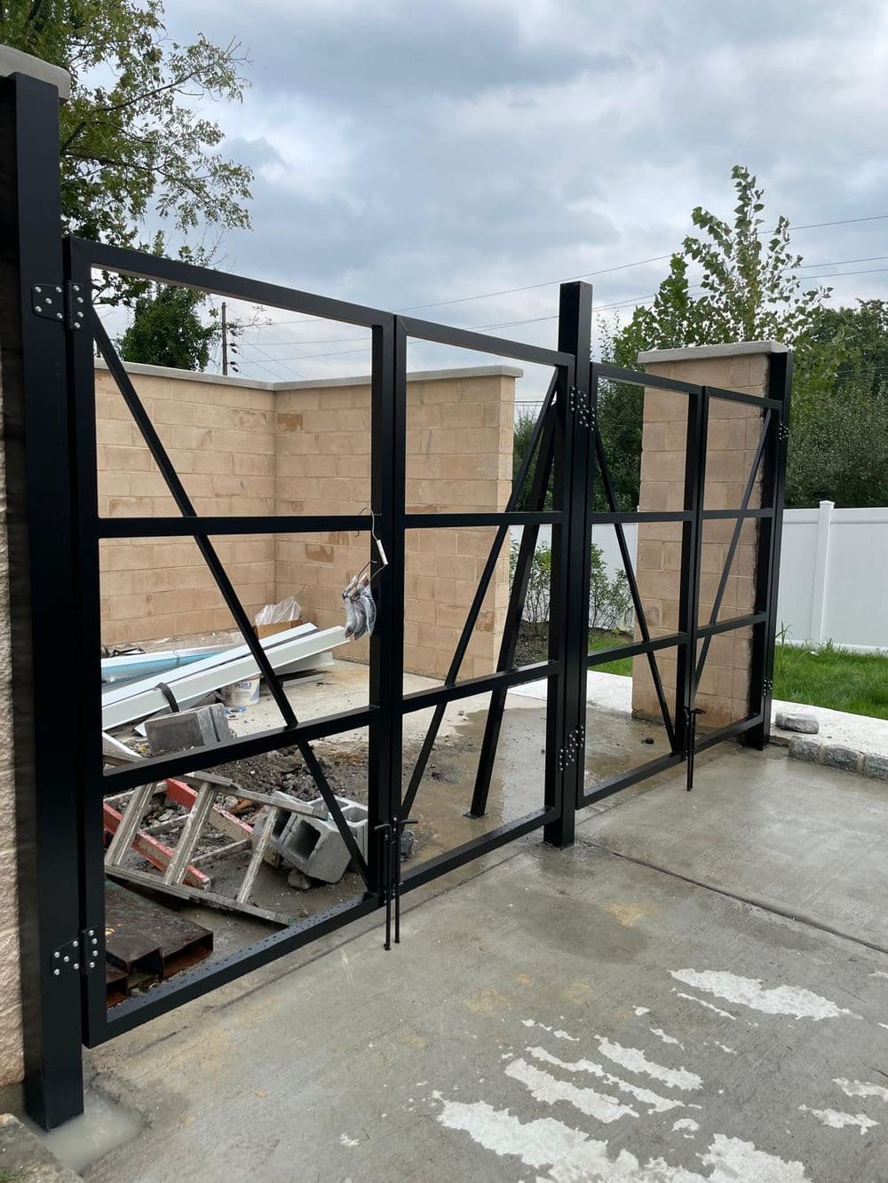 Modern black steel gate installation at a residential property entrance, with construction materials nearby.