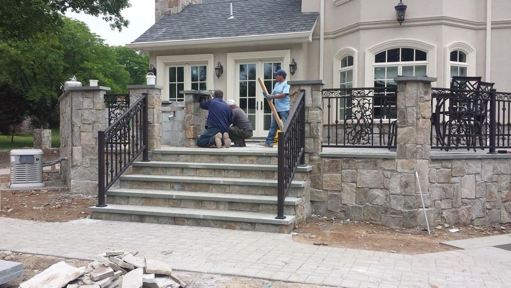 Construction workers installing stone steps and railings at a residential property entrance.