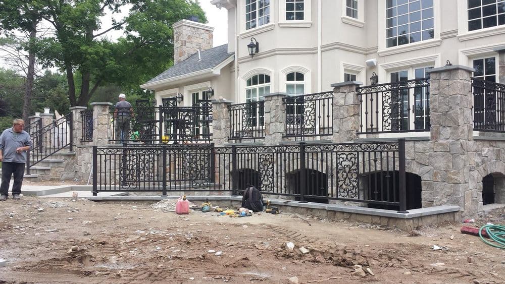 Luxury home renovation featuring stone walls and decorative iron railings under construction.