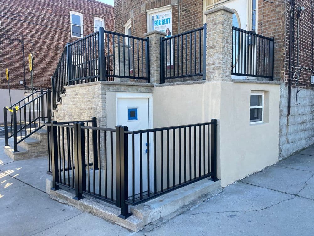 Modern building exterior with black railings and a 'For Rent' sign, featuring accessible entry.