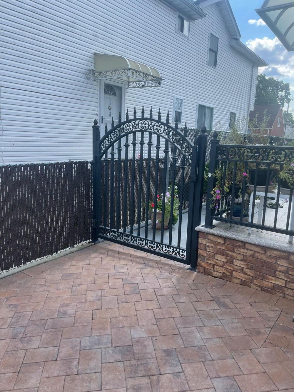 Elegant black wrought iron gate leading to a landscaped patio with pavers and flowers.