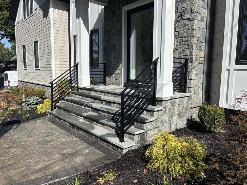 Modern stone steps with black railings and landscaped garden near a residential home.