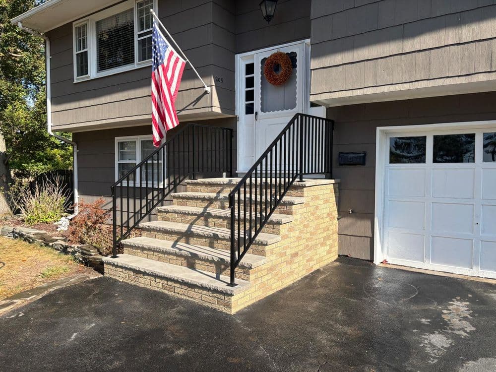 Front entrance with stairs, black railing, American flag, and welcoming fall wreath.