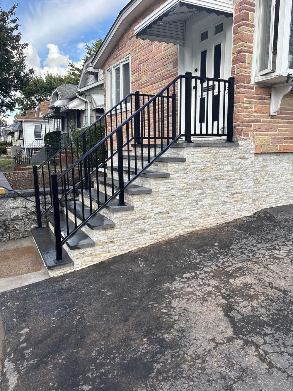 Modern outdoor staircase with black railing and stone wall, leading to a brick house.
