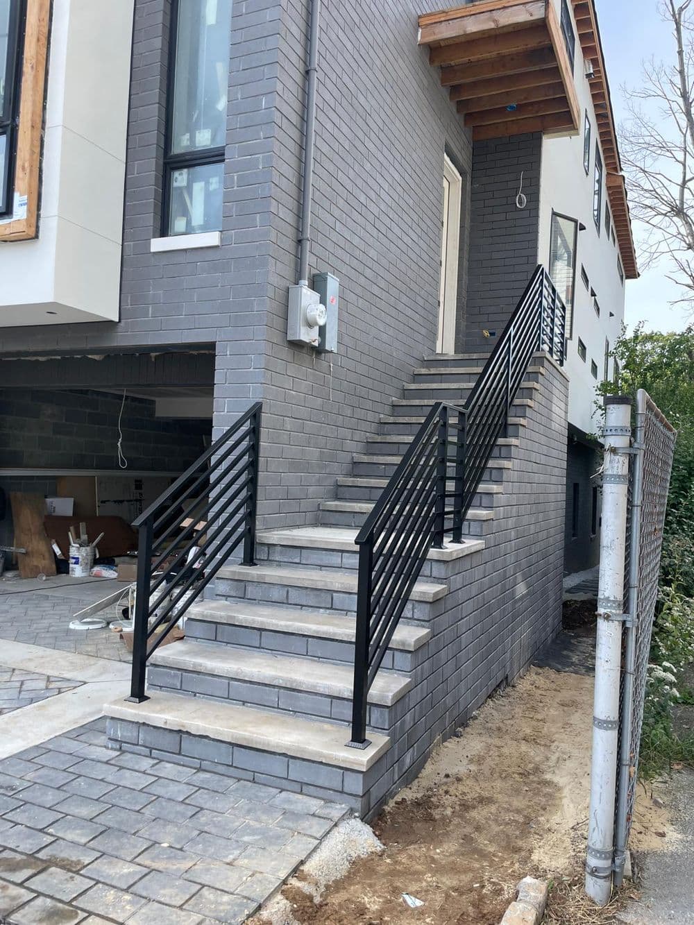 Modern brick exterior with black railing staircase leading to a newly constructed house.