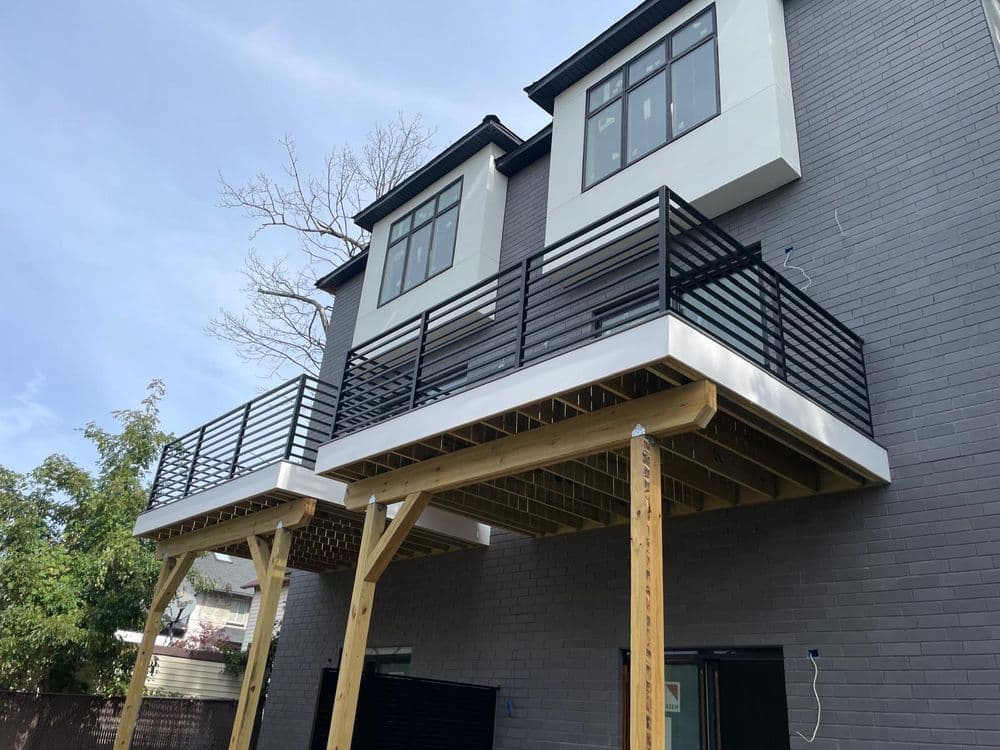 Modern two-story home with wooden balconies and black railings, featuring gray brick exterior.