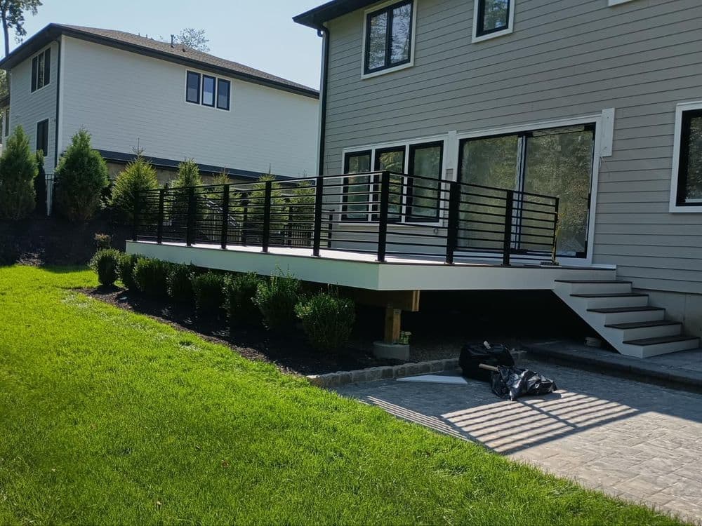 Modern backyard deck with black railing and landscaped greenery beside a contemporary house.