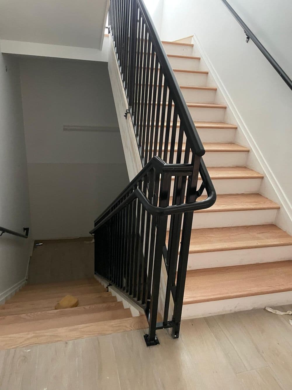 Staircase with wooden steps and black metal railing in a brightly lit interior.