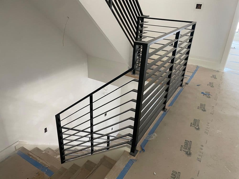 Modern black metal railing on a staircase with unfinished walls and flooring.