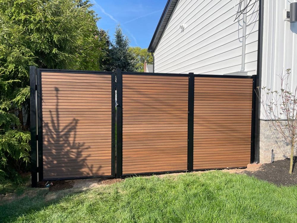 Modern wooden fence with black framing beside a house and landscaped yard.