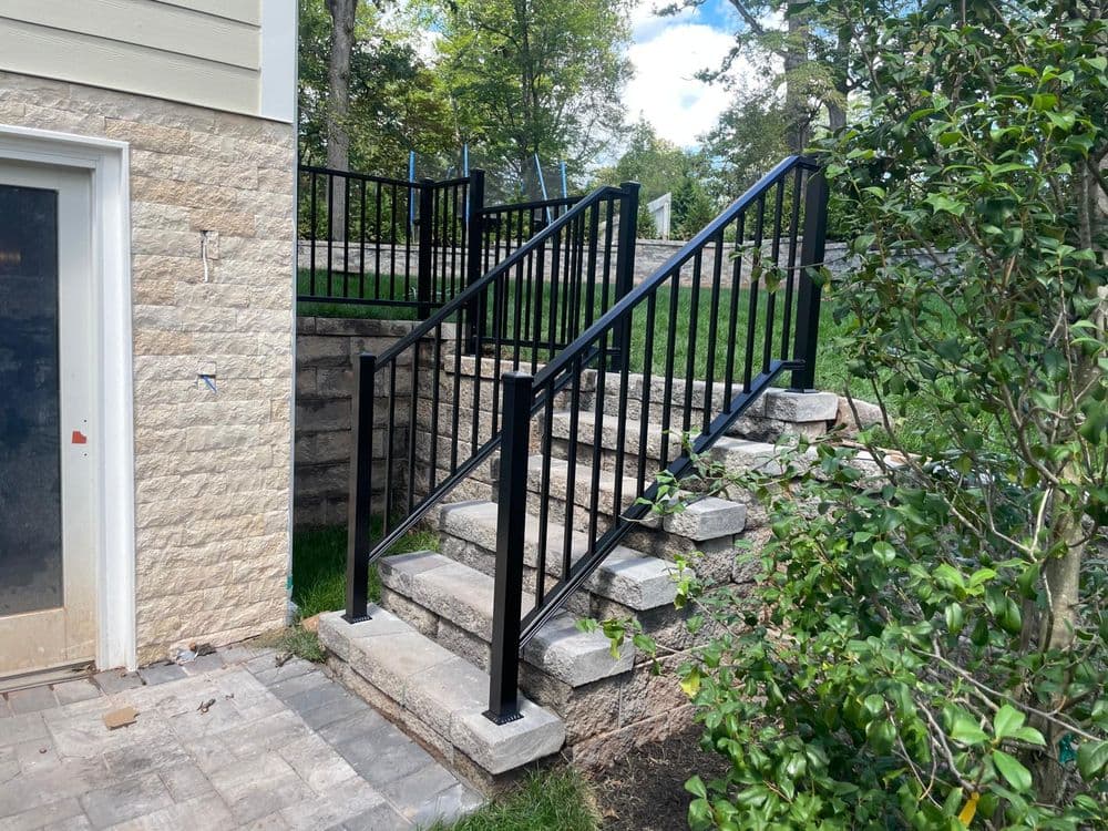 Black metal railing on stone stairs leading to a landscaped yard with green grass and trees.
