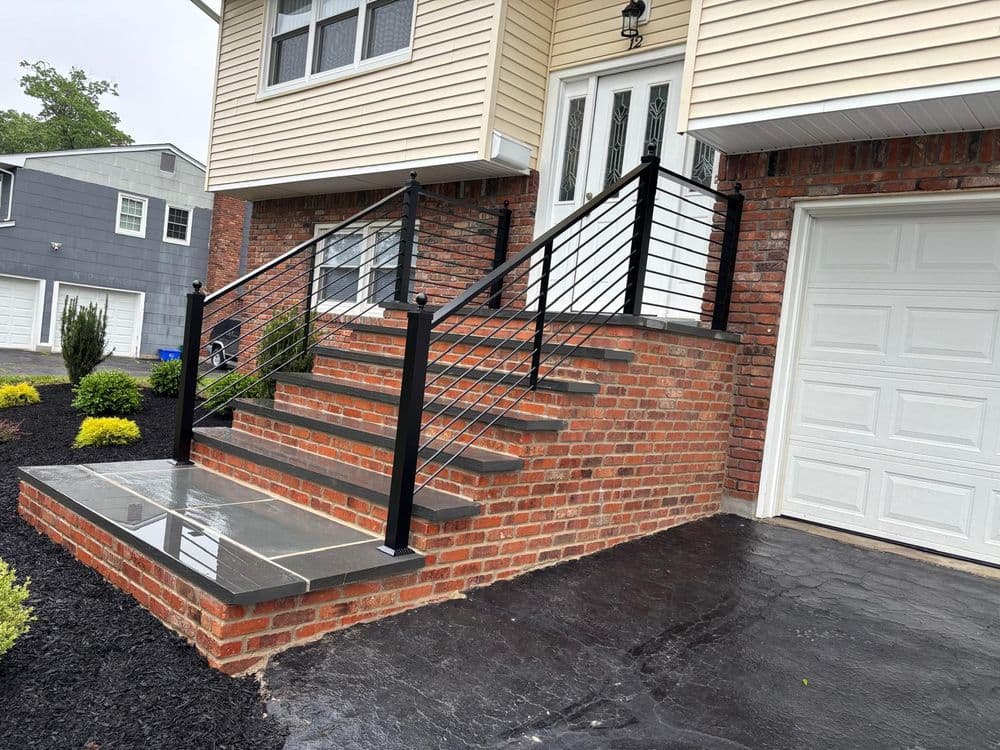 Brick staircase with modern black railing and stone landing outside a residential home.