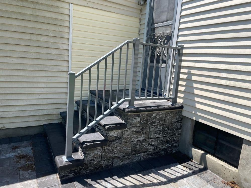 Gray handrail stairway leading to a house with textured stone steps.