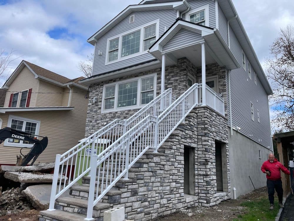 Newly constructed modern home with stone facade and white railings, featuring stairs and nearby construction.