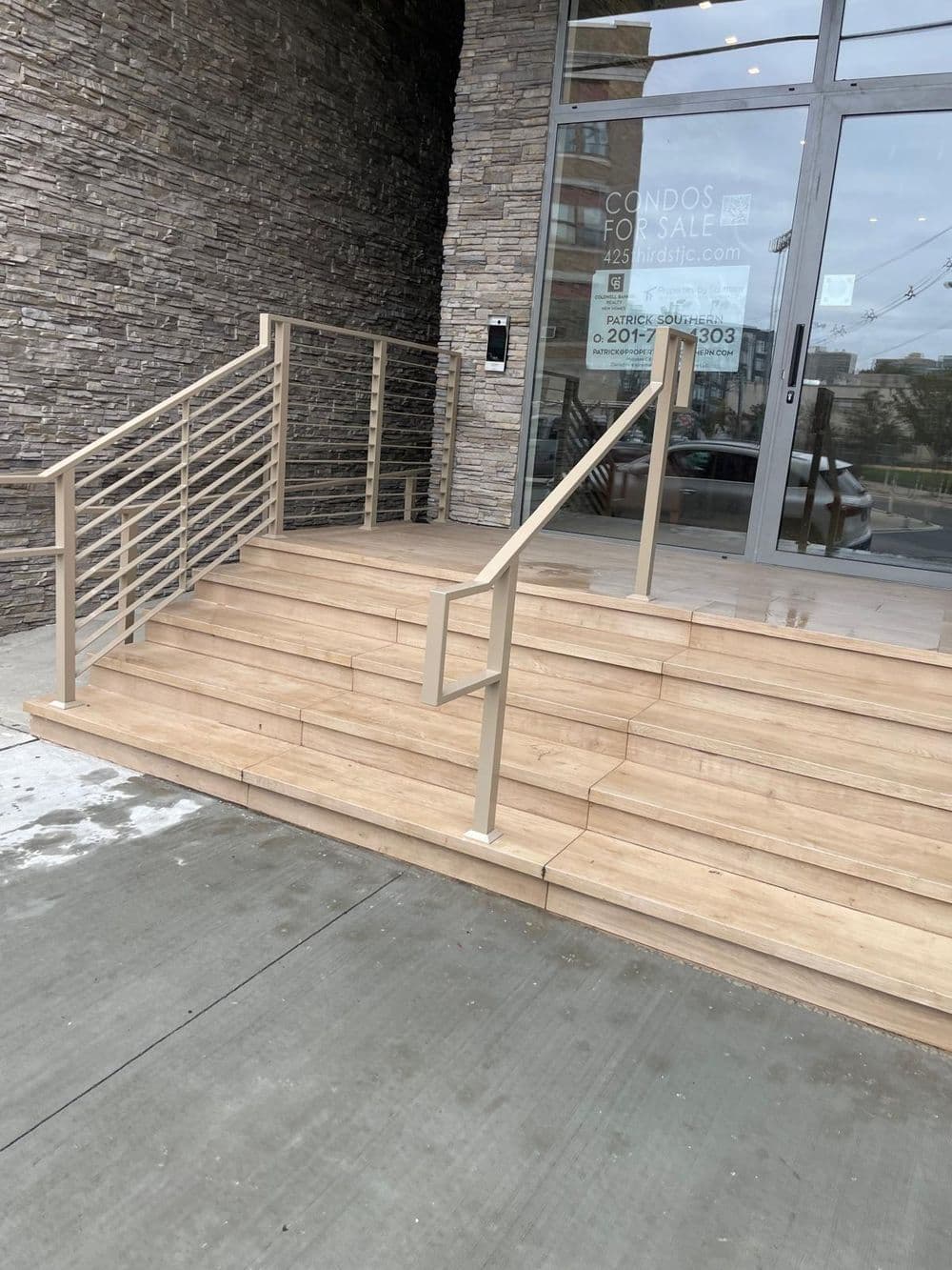 Wooden stairs with metal railing leading to a modern condo entrance with stone facade.