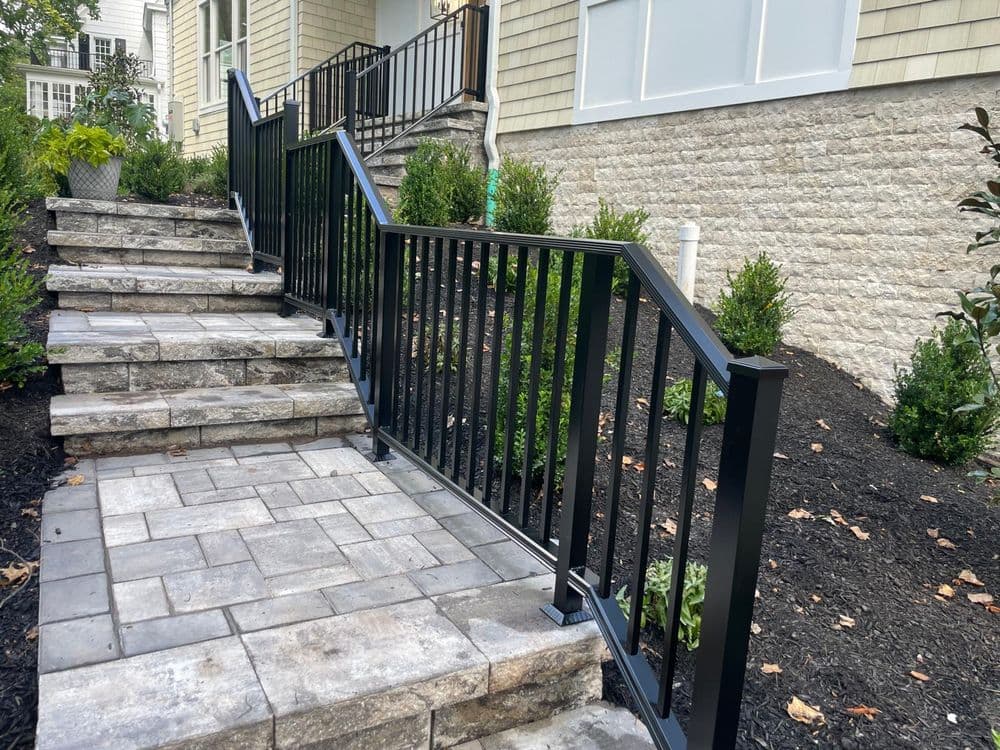 Black metal railing along stone steps leading to a modern home with landscaped garden.