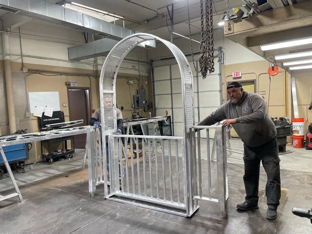 Metalworkers constructing a decorative steel garden gate in a workshop setting.
