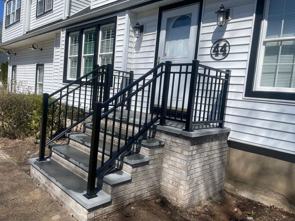 Black metal railing on concrete steps leading to a front door of a residential building.